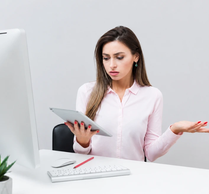 Confused businesswoman looking at a tablet while sitting at a modern office desk